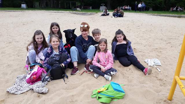 dzieci siedzą na piasku z panią i z psem