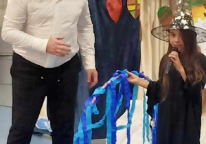 Pan Dyrektor wraz z uczennicą grającą czarownicę. Dziewczynka trzyma duże koło z niebieskimi wstążeczkami.