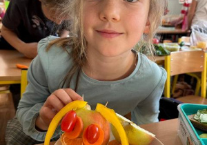 Dziewczynka prezentuje swoją pracę - głowa z jabłka, papryki żółtej, małych pomidorków.