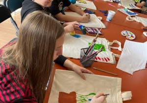 Uczniowie 5a malują farbami na torbach.