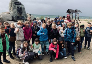 Grupa dzieci stoi przy pomniku z kamienia na najdalszym krańcu Półwyspu Helskiego