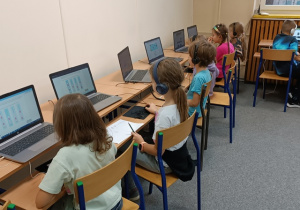 Uczniowie siedzą przy stanowiskach komputerowych i rozwiązują zadania.