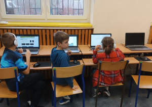 Uczniowie z klas 1-3 siedzą prze monitorami komputerów.