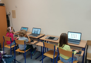Uczniowie klas 1 - 3 siedzą przy stanowiskach komputerowych.