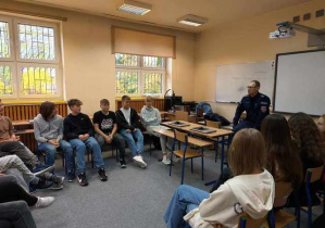 Widok na klasę i uczniów siedzących w kręgu podczas spotkania z policjantem.