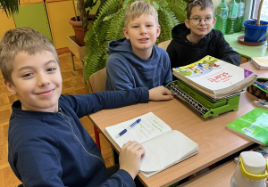 Trzech chłopców siedzi przy stoliku, używa wagi szalkowej.