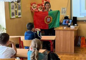 Pani prowadząca prezentuje flagę Portugalii.