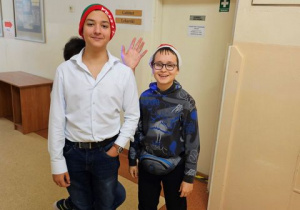 Dwóch chłopców z klasy 8a na szkolnym korytarzu w czapkach Mikołaja.