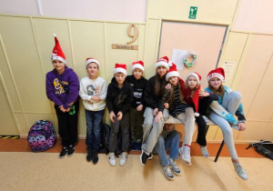 Uczniowie z 6b na szkolnym korytarzu prezentują swoje Mikołajowe czapki.