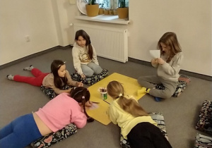 Dziewczynki leżąc na dywanie , wykonują pracę plastyczną.