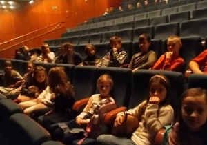 Dzieci siedzące w fotelach na widowni teatru.