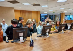 uczniowie stoją przy stanowiskach komputerowych
