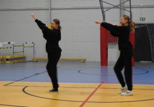 dwie dziewczyny w czarnych strojach tańczą na hali sportowej - pokaz tańca