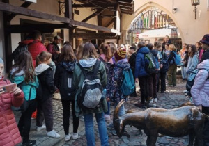 Grupa dzieci stoi w wąskiej uliczce, tuż koło nich postacie zwierząt - koza, świnia