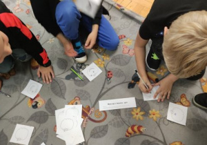 chłopcy siedzący na dywanie, rysują dynie na karteczkach