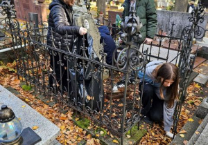 Grupa uczniów porządkująca zabytkowe nagrobki.