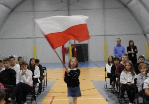 uczennica idąca środkiem sali z biało-czerwoną flagą