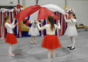 cztery dziewczynki w biało-czerwonych strojach tańczą układ z biało-czerwonymi chustami