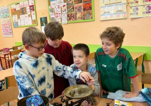 Grupa chłopców sprawdza wagę róznych przedmiotów przy użyciu wagi szalkowej.