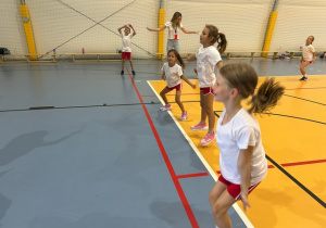Dzieci wykonujące ćwiczenia w hali sportowej.
