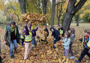 Uczniowie podrzucają do góry jesienne liście.