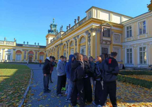 Uczniowie stoja w ogrodzie przed pałacem w Wilanowie.