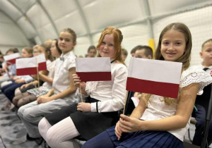 Uczniowie z flagami podczas uroczystości szkolnej.