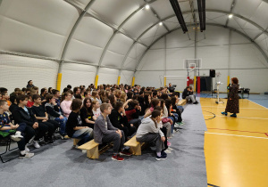 Młodzież szkoły zgromadzona w hali sportowej podczas spotkania.