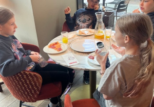 Grupa uczniów, siedząca przy stoliku w pizzerii.