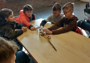 Dzieci siedzące za stołem na warsztatach, trzymają gałązkę bawełny