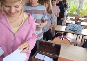 Uczniowie z kartkami podchodzą do skrzynki.