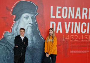 Para uczniów pozuje na tle wielkiego plakatu Leonardo da Vinci