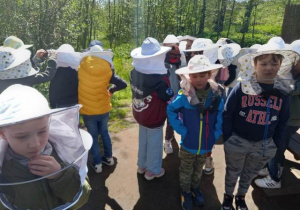Dzieci w strojach pszczelarzy obserwują życie pszczół