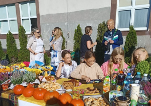 Stoisko piknikowe z ciastami, w tle rodzice i uczniowie.
